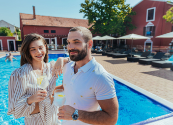 A man and a woman standing by the pool and toasting with drinks
