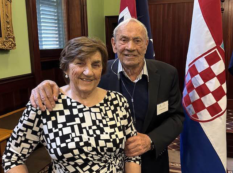 Dvoje ljudi poziraju u interijeru uz državnu zastavu