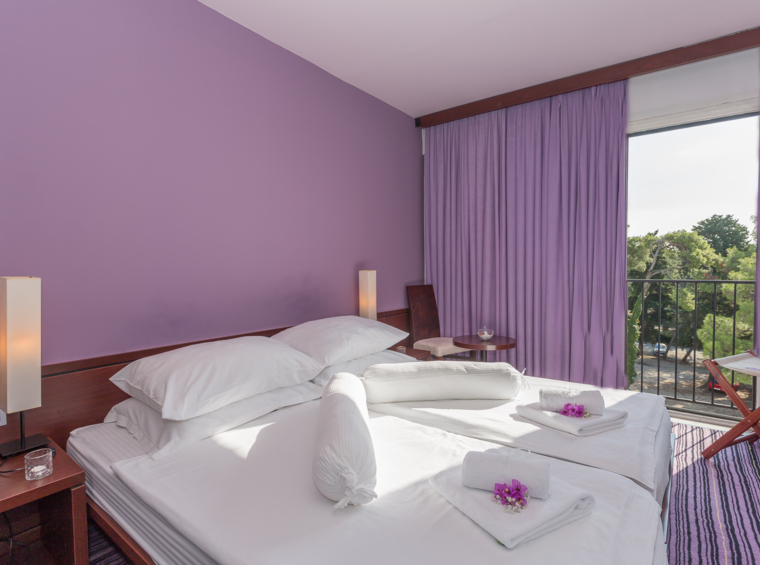 Hotelska soba s ljubičastim zidovima, bračnim krevetom i balkonom