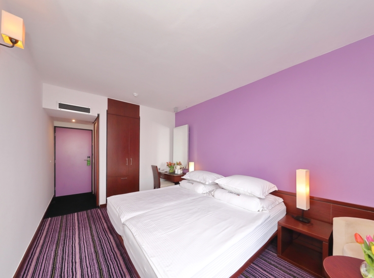 Hotelska soba s ljubičastim interijerom i udobnim bračnim krevetom