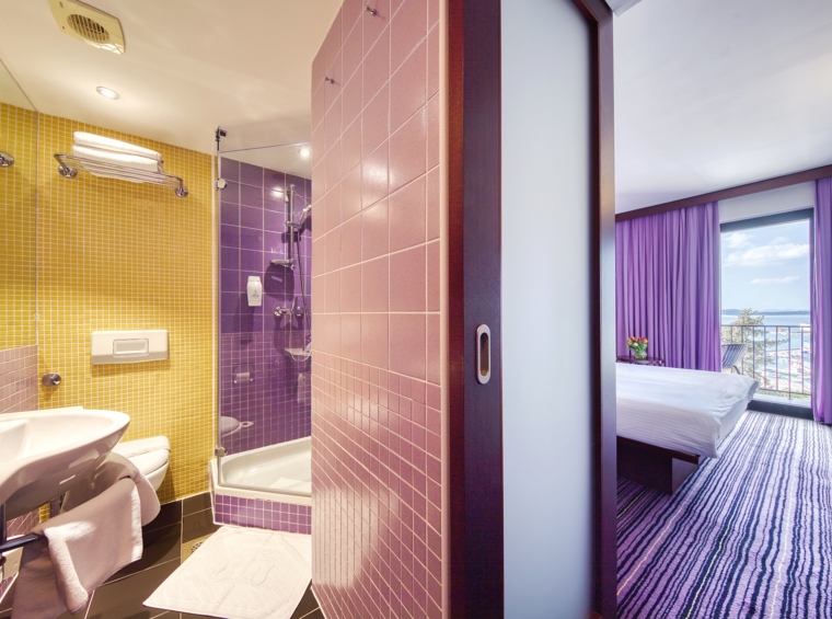 modernes hotelbad mit dusche und schlafzimmer mit blick auf die stadt