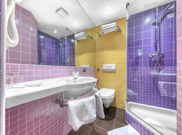 modernes hotelbad mit badewanne und dusche in lila-gelben fliesen