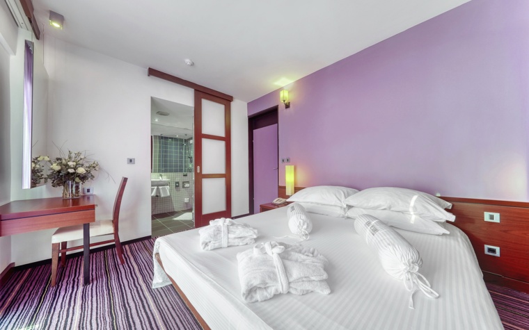 svijetla hotelska soba s bračnim krevetom u ljubičastim tonovima