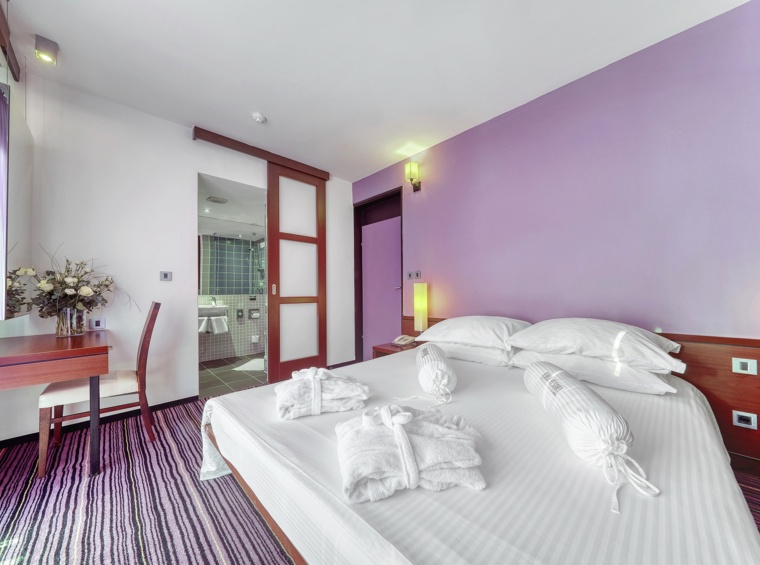 svijetla hotelska soba s bračnim krevetom u ljubičastim tonovima