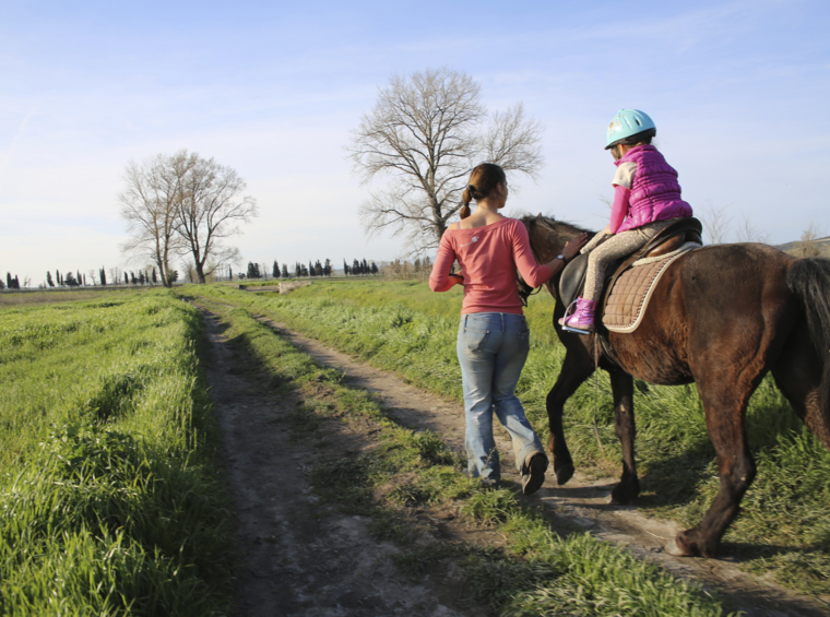 child riding a horse with an instructor
