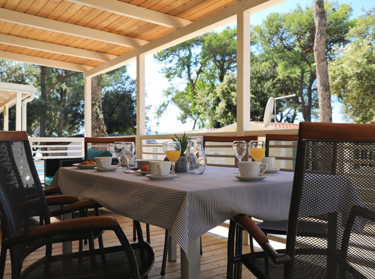 Natkrivena terasa s blagovaonskim stolom u sjeni borova