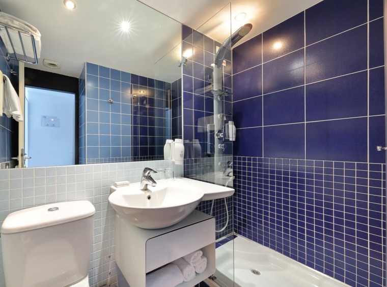 Hotelska kopalnica s prho, umivalnikom in modrimi keramičnimi ploščicami