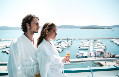 Muškarac i žena stoje na balkonu u kućnim ogrtačima s pogledom na marinu