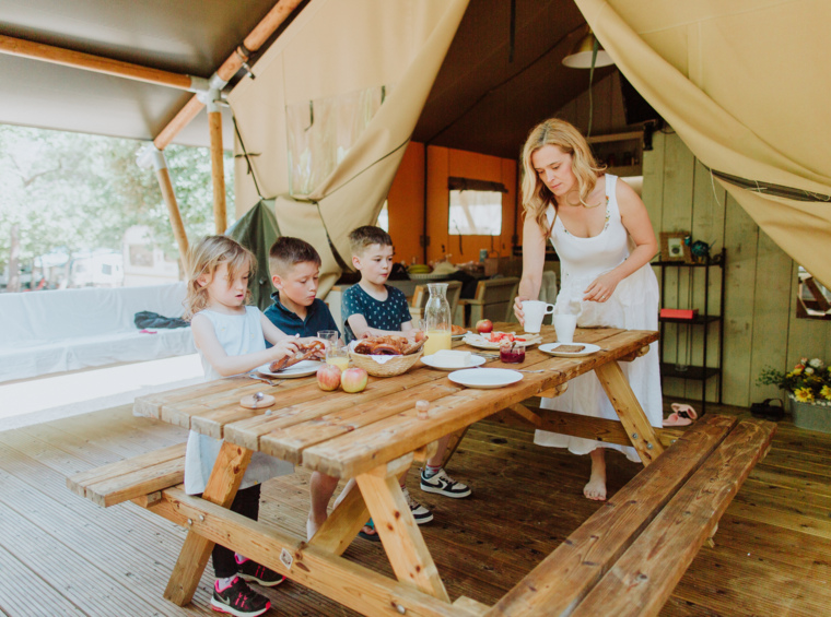 Mother and children sitting at a table inside a glamping tent