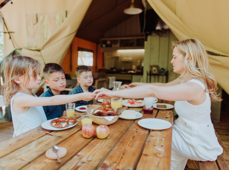 A woman serving a meal to children at a wooden table in a glamping tent